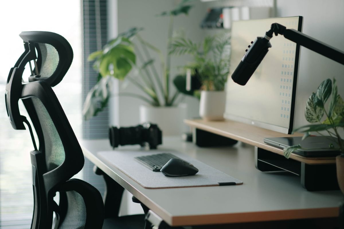 A monitor arm holding a screen above a tidy desk with a plant